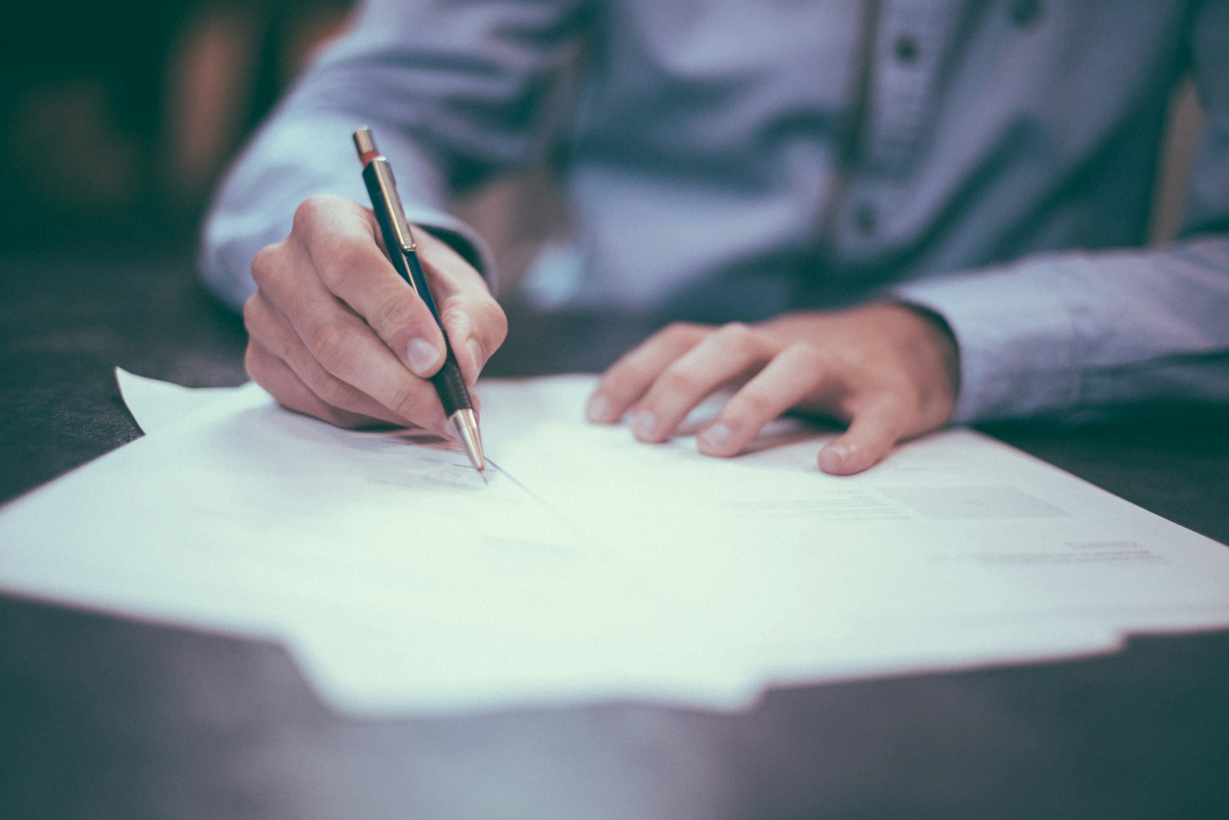 Fountain pen signing financial documents on a dark desk